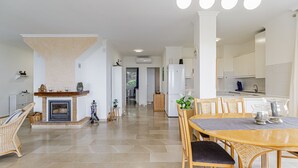 Een ruime woonkamer met een open haard, een eettafel en een keuken op de achtergrond.