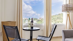Een kamer met uitzicht op de lucht en groen, een ronde tafel met twee stoelen, twee wijnflessen en twee glazen.
