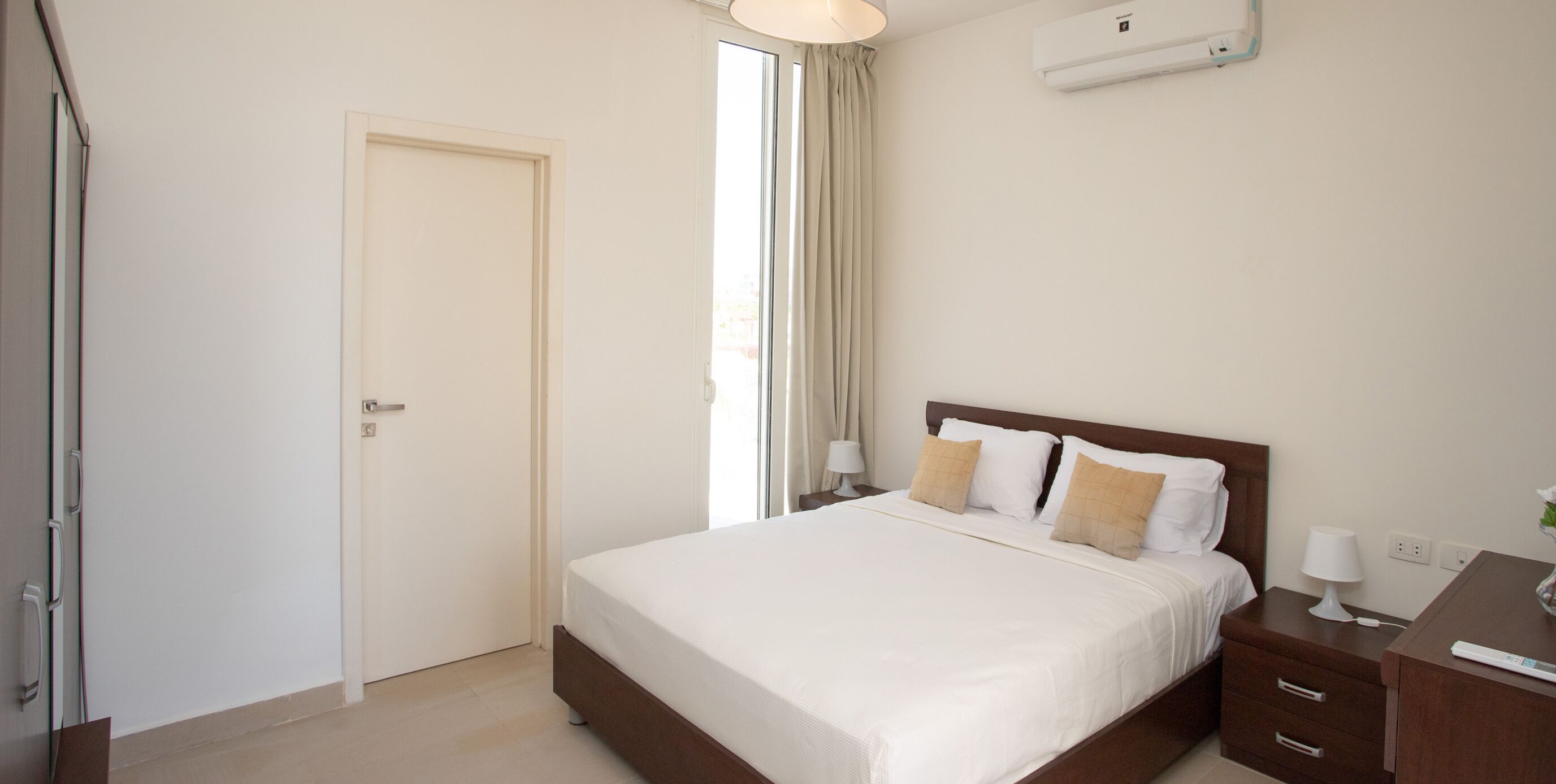 A bedroom with a bed, bedside tables, a nightstand, a dresser, and an air conditioning unit.