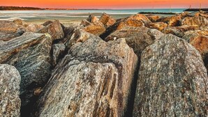 Eine felsige Küstenlinie mit großen Felsen und ein weiter Blick auf einen Leuchtturm.