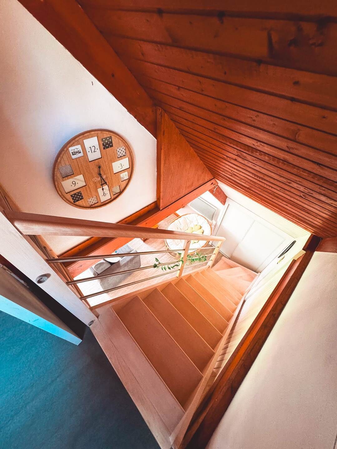 Uma escada de madeira leva a um quarto com um relógio no teto e vista para o exterior.