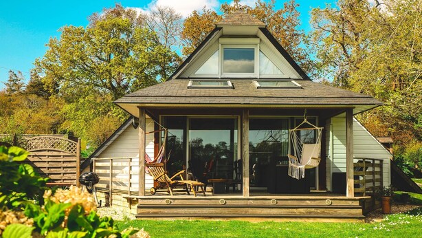 Ein Haus mit einer großen Veranda, einem überdachten Sitzbereich und Blick auf die umliegenden Bäume.