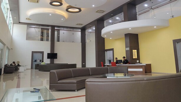 A modern lobby with a curved reception desk, seating areas, and a glass coffee table. - Praveg Rezort Silvassa (Silvassa)