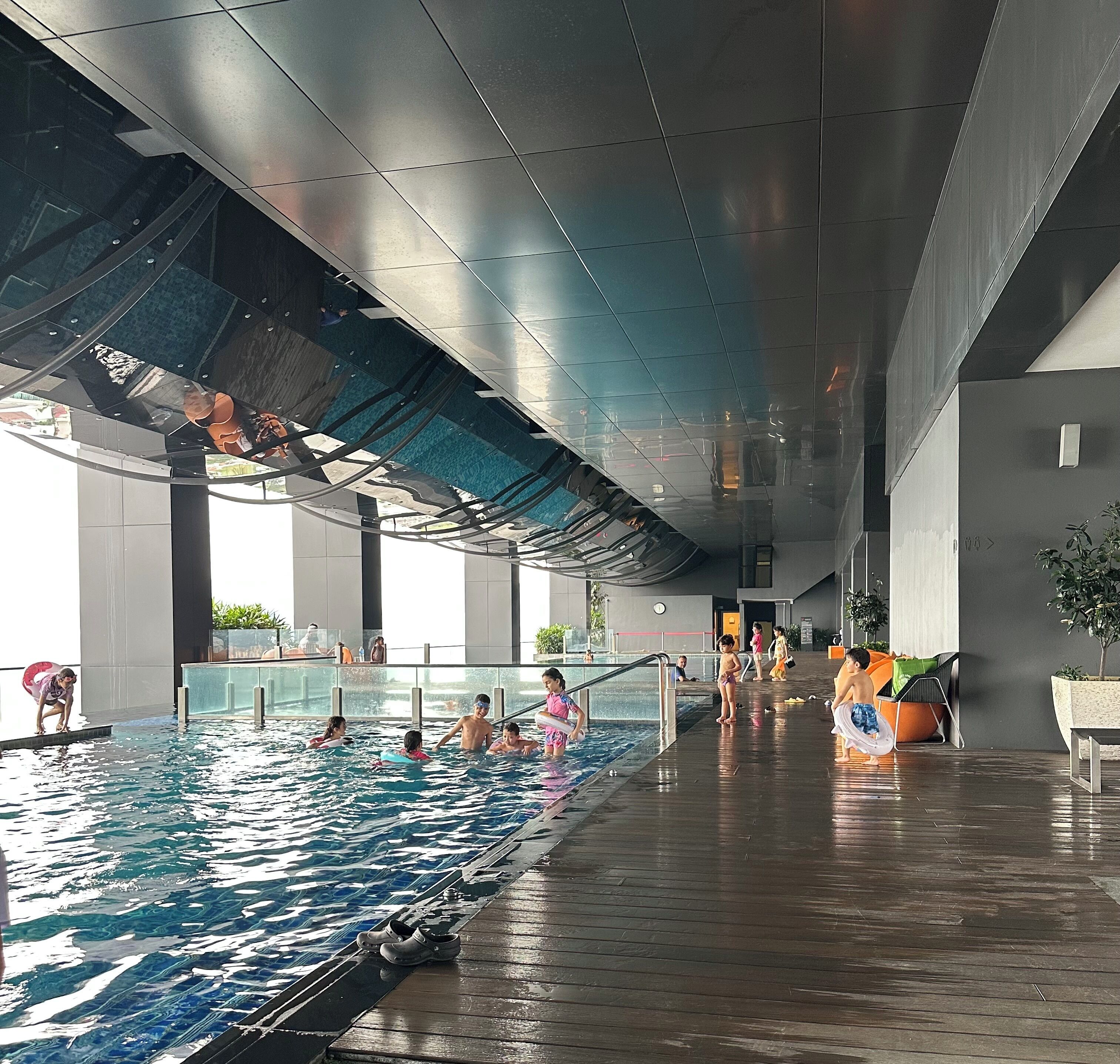 An indoor swimming pool with clear water, surrounded by a modern architectural design with large windows and a covered area.