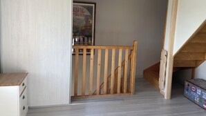 A room with a wooden staircase, a white wall, and a poster on the wall.