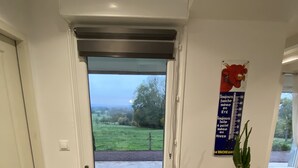 A modern kitchen with a built-in oven, a dining area with a wooden table and chairs, and a view of a green landscape through an open door.
