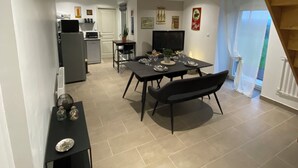 A spacious living area with a dining table set for four, a kitchen in the background, and a staircase leading to an upper floor.