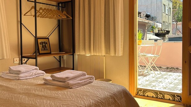 Ein Schlafzimmer mit Bett, Holzboden, Fenster mit Vorhängen, Heizkörper und Blick ins Freie.