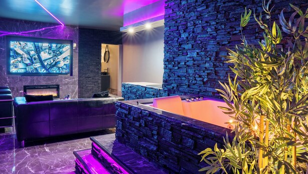 A modern spa area with a stone wall, a large bathtub, and a reception desk. - The Floor - Ombre D'Ebene Loft & private Jacuzzi (Coignières)
