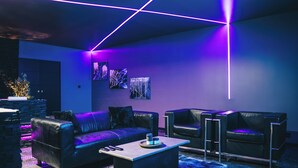 A modern living room with a black leather sofa, a coffee table, and a black leather armchair. There are abstract paintings on the wall and a stone fireplace. - The Floor - Ombre D'Ebene Loft & private Jacuzzi (Coignières)