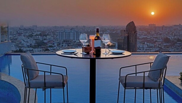 Une table dressée pour deux personnes, avec une bouteille et des verres, donnant sur une vue panoramique de la ville au coucher du soleil.