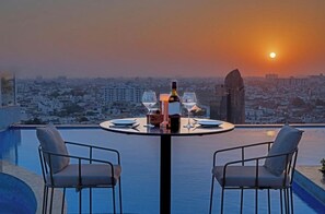 Mesa para dos con una botella y vasos, con vista a un paisaje urbano al atardecer.
