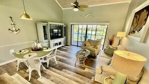A spacious living room with a dining area, a television, and a large window overlooking a deck.