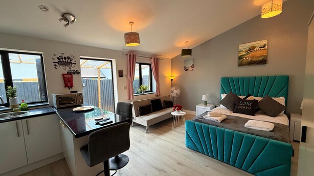 A compact hotel room with a kitchenette, a sofa, a bed with teal headboard, and a small dining area. - 526A Farnham Rd  (Slough)