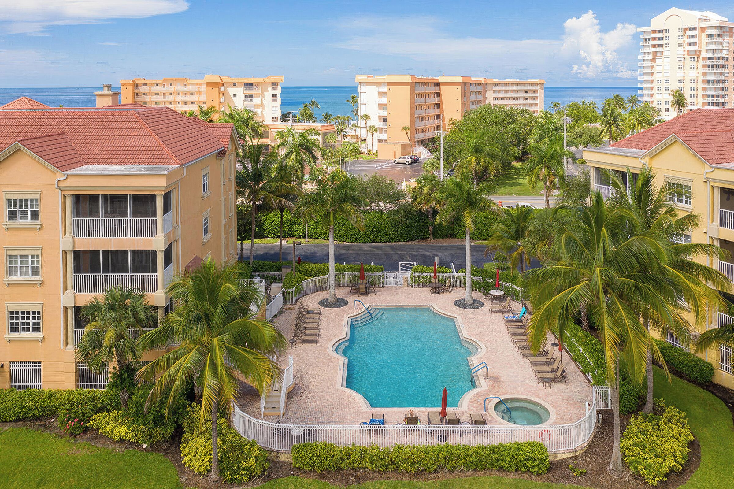 Ein Resort mit einem zentral gelegenen Schwimmbad, umgeben von Palmen und Blick auf den Ozean.
