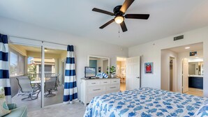 Un dormitorio con cama, escritorio, silla, ventilador de techo y vistas a un balcón.
