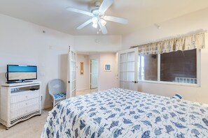 A bedroom with a bed, a television, a ceiling fan, and a window with curtains.