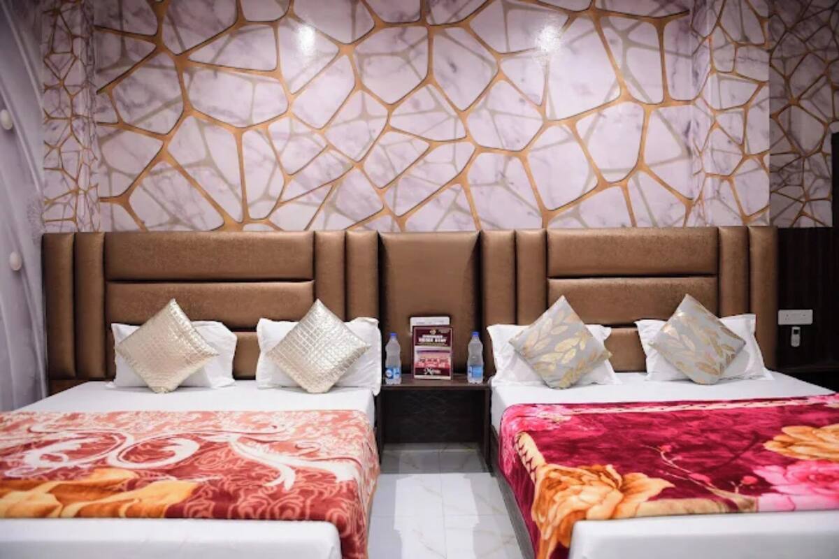 Een hotelkamer met twee bedden, een wand met een marmerlook en een nachtkastje met een fles water en een doos.