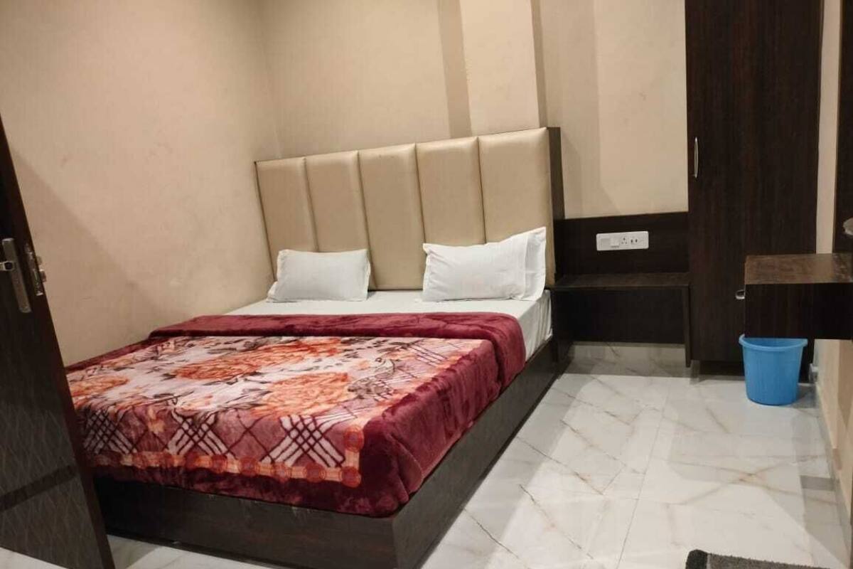 Een slaapkamer met een bed, een hoofdeinde, een nachtkastje, een blauwe prullenbak en een deur naar de badkamer.