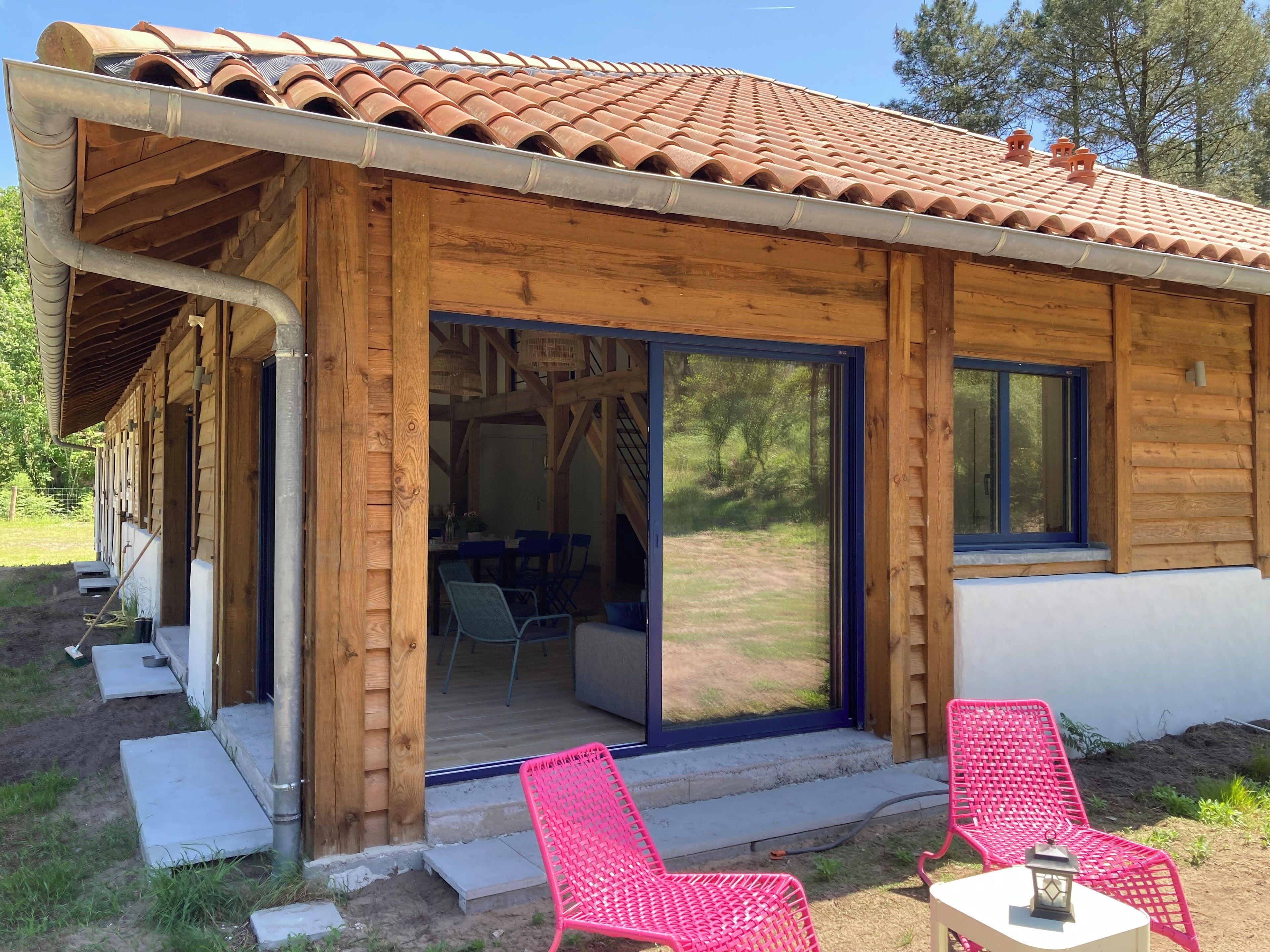 Eine Holzhütte mit Ziegeldach, großen Schiebeglastüren und einer Terrasse mit zwei Stühlen und einem Tisch.