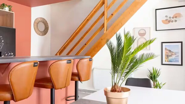 Una cocina moderna con una escalera de madera, una zona de comedor con sillas de cuero y una planta en maceta.