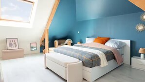 Un dormitorio con techo inclinado, una cama con colcha a rayas, un banco y una mesita de noche con una lámpara.