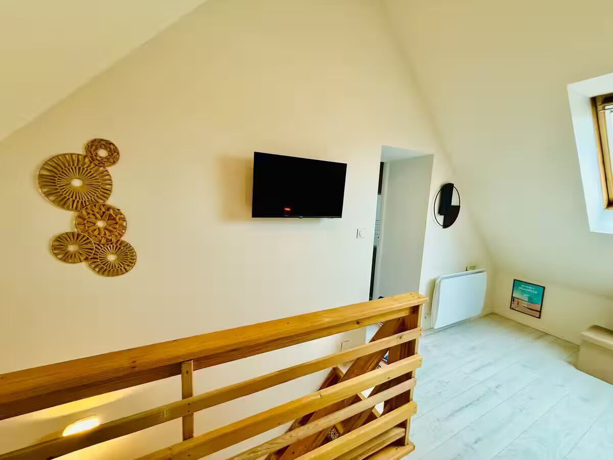 Une pièce spacieuse avec un escalier en bois, un téléviseur à écran plat fixé au mur et un élément décoratif mural.