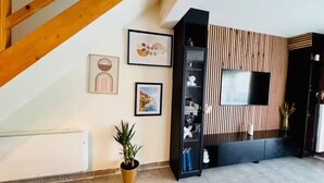 Una sala de estar moderna con una escalera de madera, un televisor de pantalla plana montado en una pared de paneles de madera y una planta en maceta.