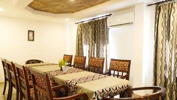 Uma sala de jantar com uma mesa comprida, toalha de mesa estampada, cadeiras de madeira e cortinas.