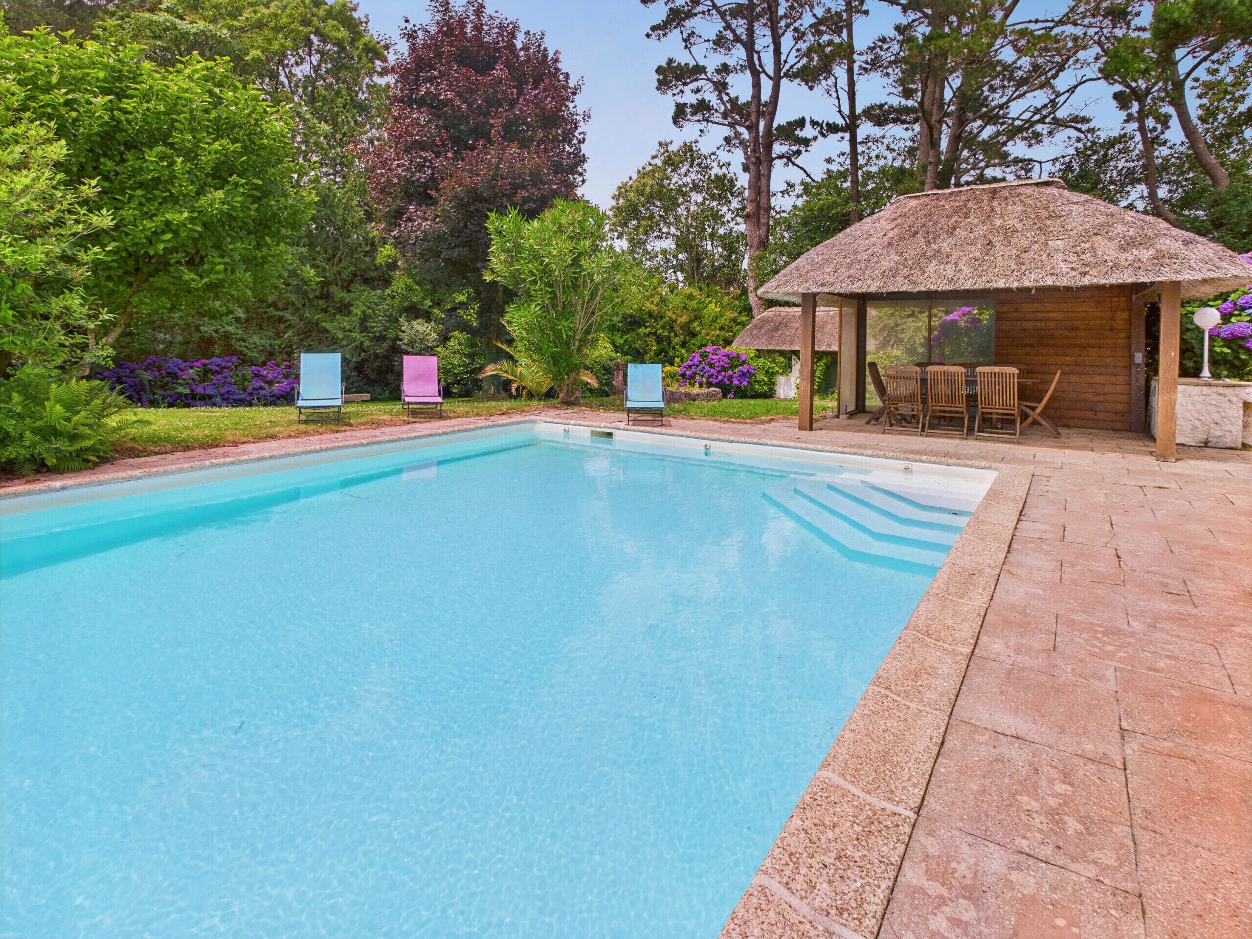A swimming pool with a wooden deck and a thatched-roof pavilion.