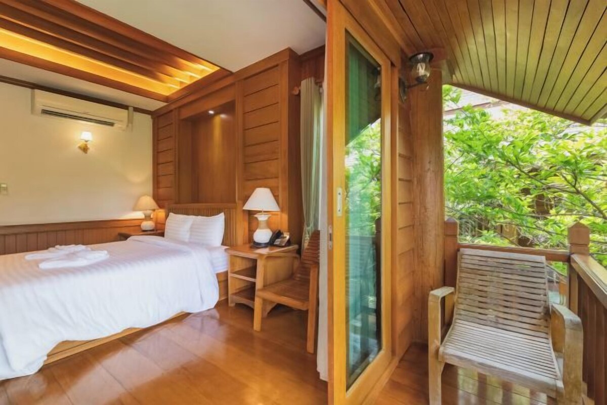A wooden room with a bed, bedside tables, and a window overlooking greenery.