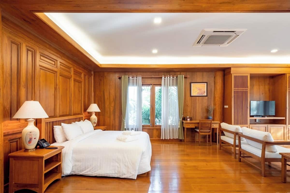 A spacious hotel room with a large bed, wooden paneling, a desk with a chair, a TV, and a seating area with a sofa and armchairs.