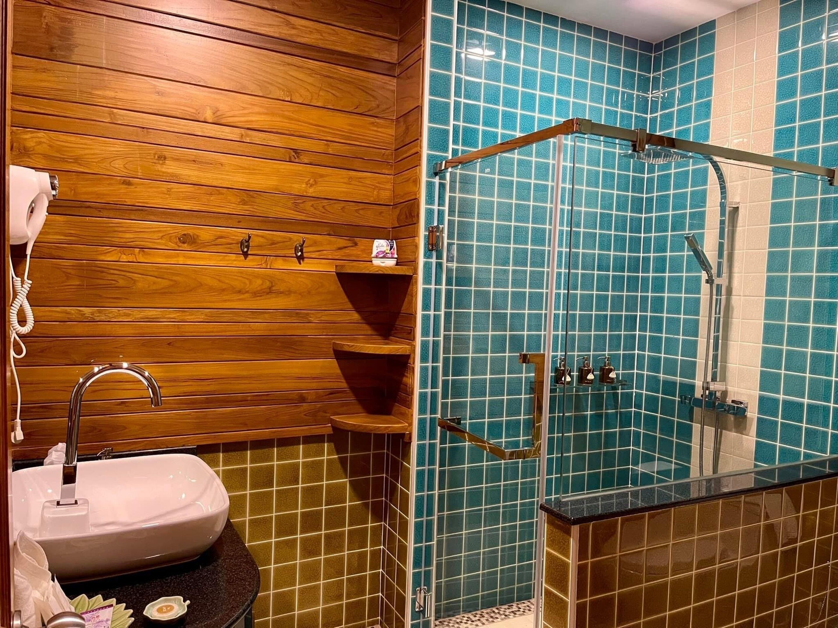 Een badkamer met een houten wastafelmeubel, een wastafel en een douchegedeelte met blauwe tegels.