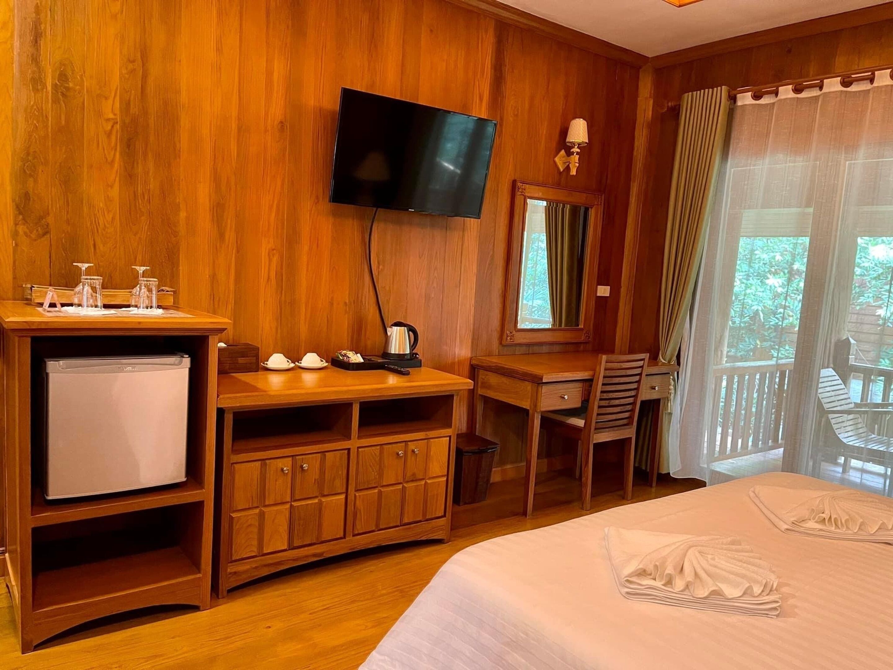 Een houten kamer met een bed, een bureau, een stoel, een televisie en een raam met gordijnen.