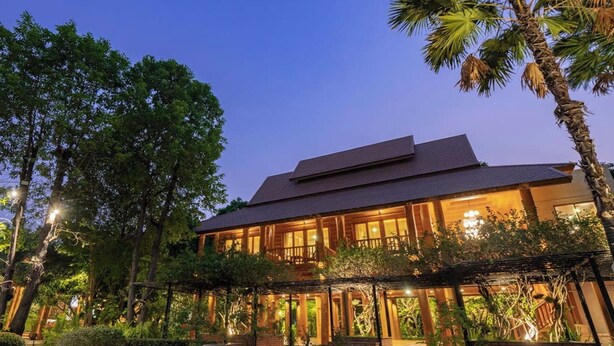 A two-story building with a flat roof and large windows, surrounded by lush greenery and palm trees. - Vanasin Residence (Tak)