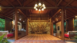 A covered outdoor area with a tiled floor, wooden pillars, and a central seating area with a decorative plant arrangement. - Vanasin Residence (Tak)