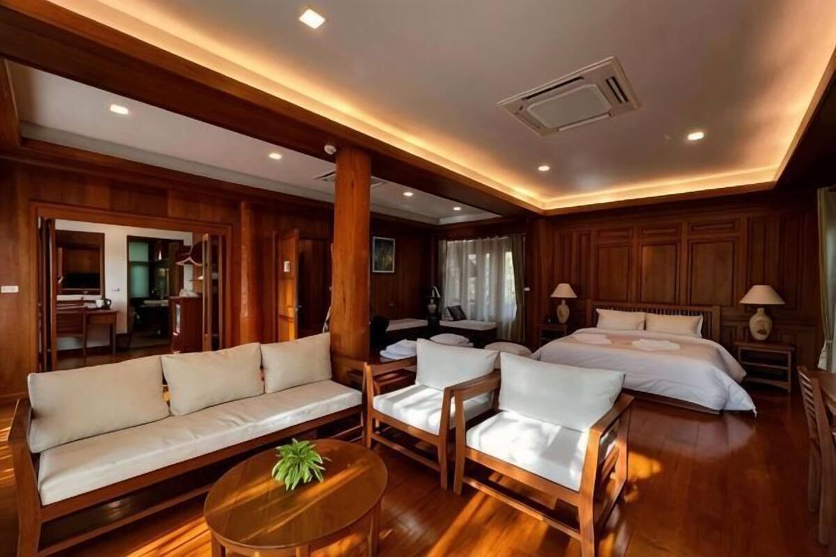 A hotel room with a wooden floor, a sofa, a bed, a chair, a table, and a lamp.