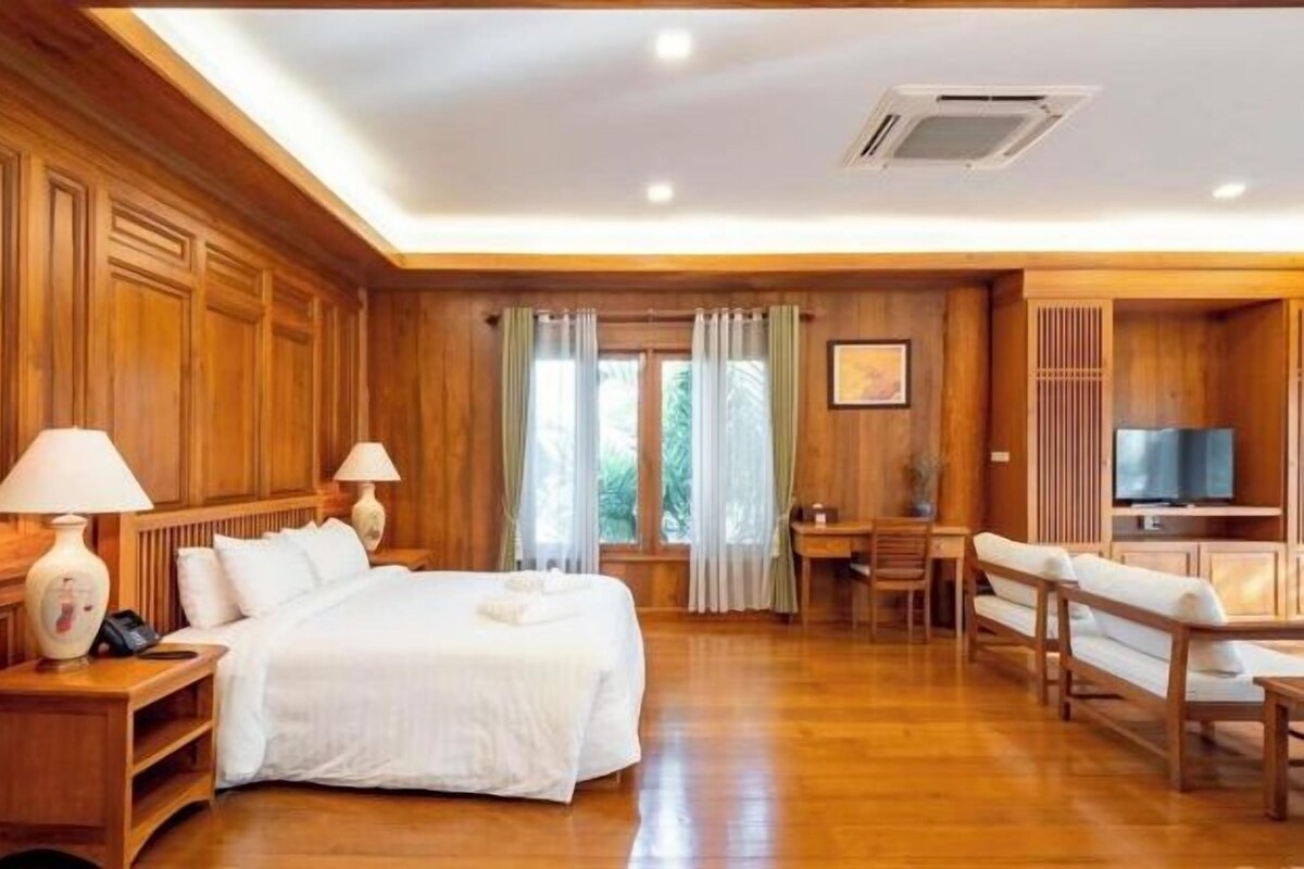 A hotel room with a wooden interior, a bed, a desk, a chair, a television, and a window with curtains.