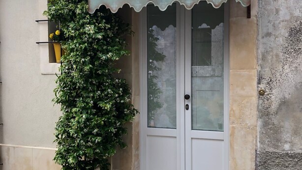 A building with a white door and a small awning. There is a large potted plant with white flowers next to the door. - La Casa Dell'Artista - Short Term Rentals - Ferla (Ferla)