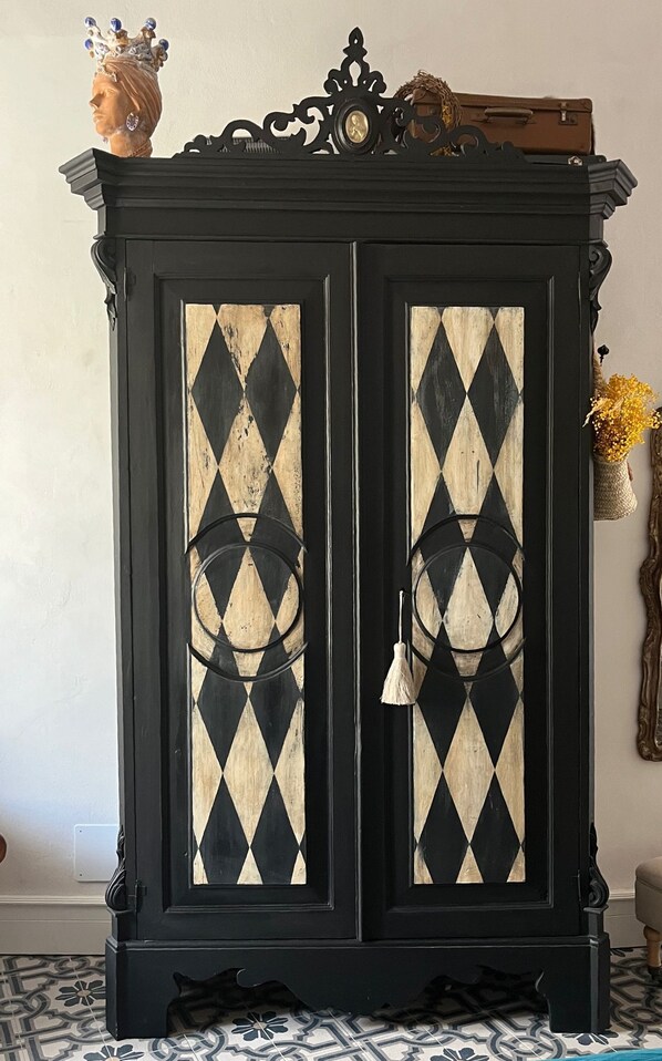 A black cabinet with diamond-patterned glass doors, a small statue on top, and a vase with flowers to the right.