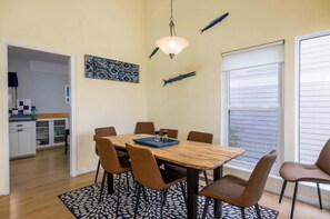 Uma sala de jantar com mesa de madeira, cadeiras marrons, luminária pendente e peixes decorativos na parede.