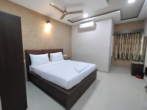 Een moderne hotelkamer met een groot bed, plafondventilator, wandairconditioner en een raam met gordijnen.