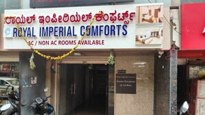 A hotel entrance with a sign for "Royal Imperial Comforts" offering both AC and non-AC rooms. A "No Parking" sign is visible, and the reception is on the 1st floor. - PPH Living Royal Imperial Comforts (Bengaluru)