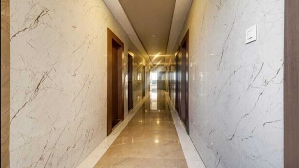 A long, narrow hallway with marble walls and a shiny floor, leading to a bright area at the end. - PPH Living Royal Imperial Comforts (Bengaluru)