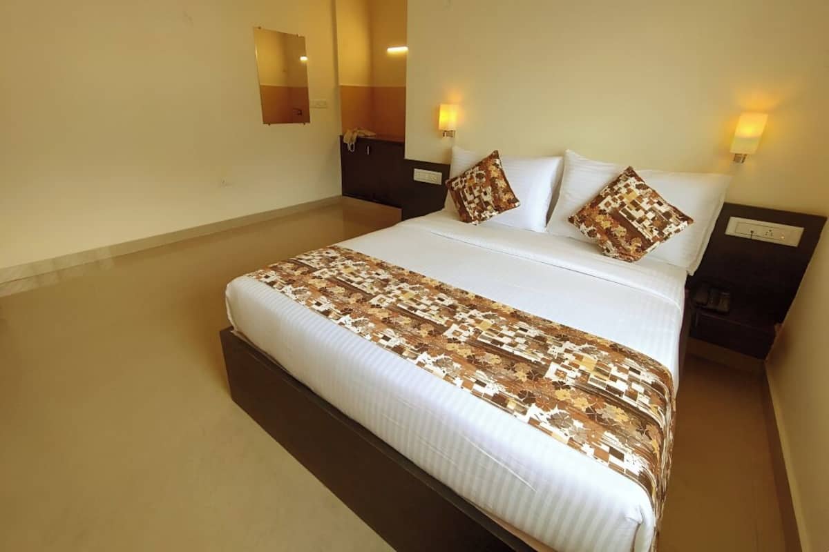 A hotel room with a large bed, two bedside tables, a nightstand, a mirror, and two wall-mounted lamps.