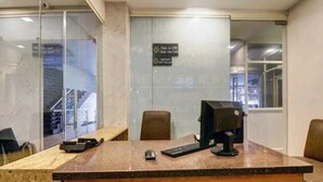 A reception desk with a computer, a mouse, and a keyboard. There are chairs and a glass partition. - PPH Living Royal Imperial Comforts (Bengaluru)