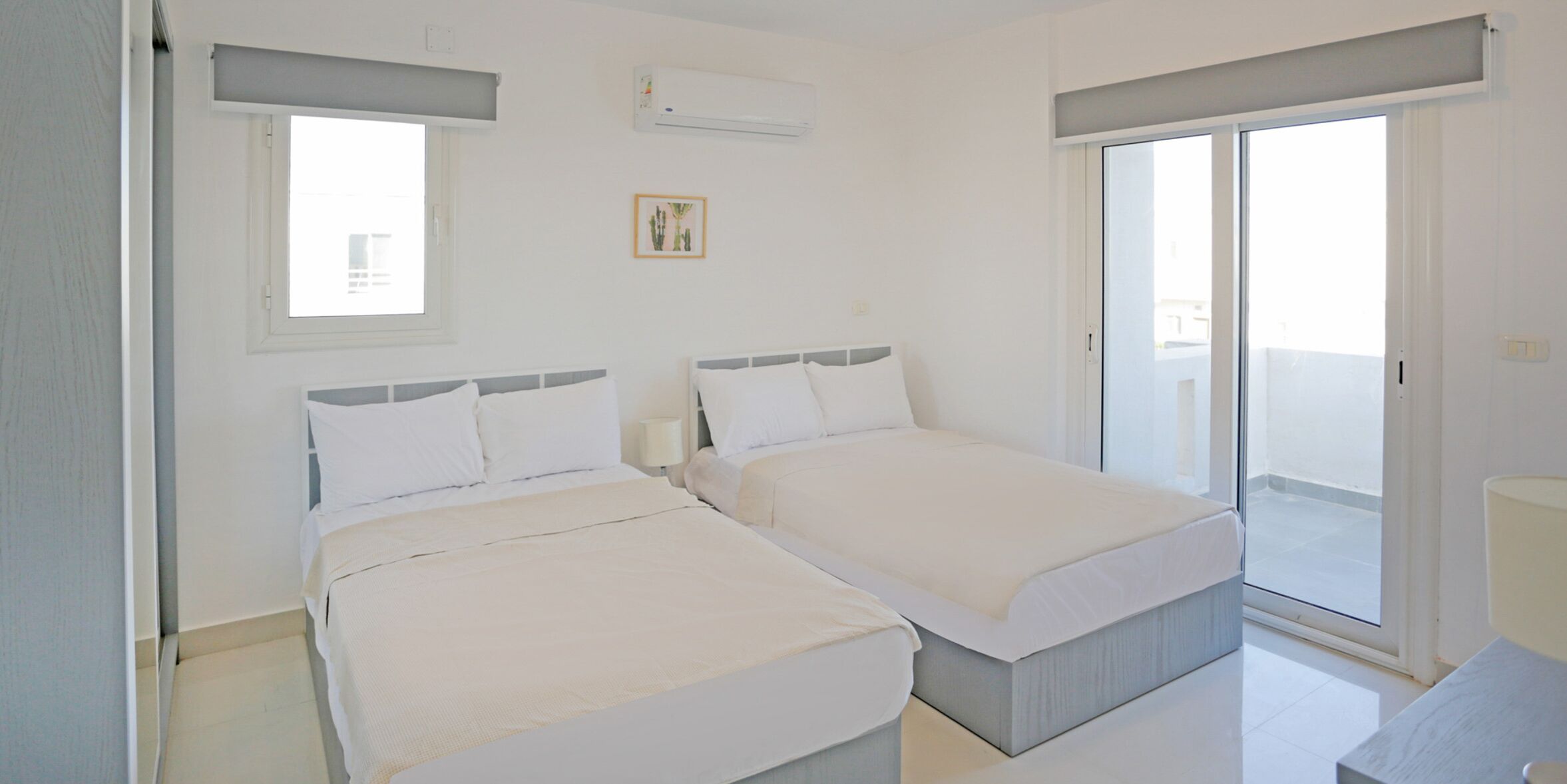 A bedroom with two beds, a window, an air conditioner, and a door leading to a balcony.
