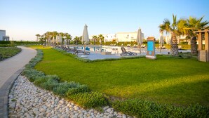 A poolside area with lounge chairs, a signboard, and palm trees. - Prime Holidays Amwaj (El Alamein)