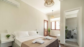 A modern bedroom with a large bed, bedside tables, a bedside plant, and a view into the bathroom. - Casa Chris (Chania)