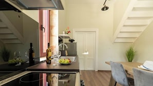 A modern kitchen with a central island, a dining area with a wooden table and chairs, and a staircase leading to an upper level. - Casa Chris (Chania)
